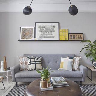 grey living room with a wall-mounted shelf topped with picture frames above a grey sofa with patterned pillows and multiple coffee tables with accessories