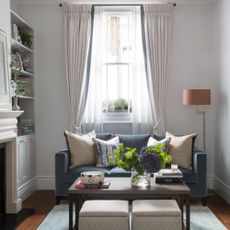A narrow white living room with a small blue velvet sofa positioned away from the wall