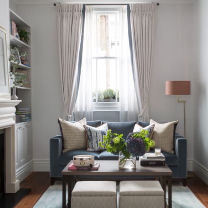 A narrow white living room with a small blue velvet sofa positioned away from the wall