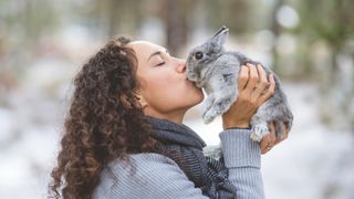 A woman holds up a little bunny and kisses her. They&#039;re outside in the woods on a chilly winter afternoon.