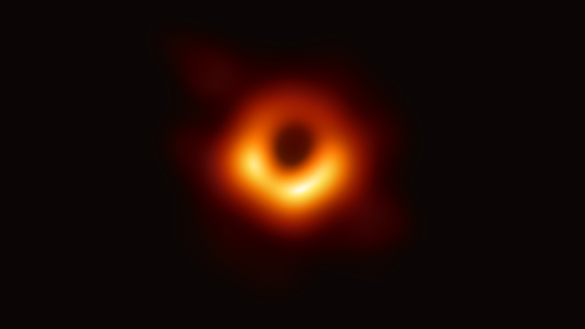 Image of black hole looks like a bright orange glowing ring with dark patch in the center.