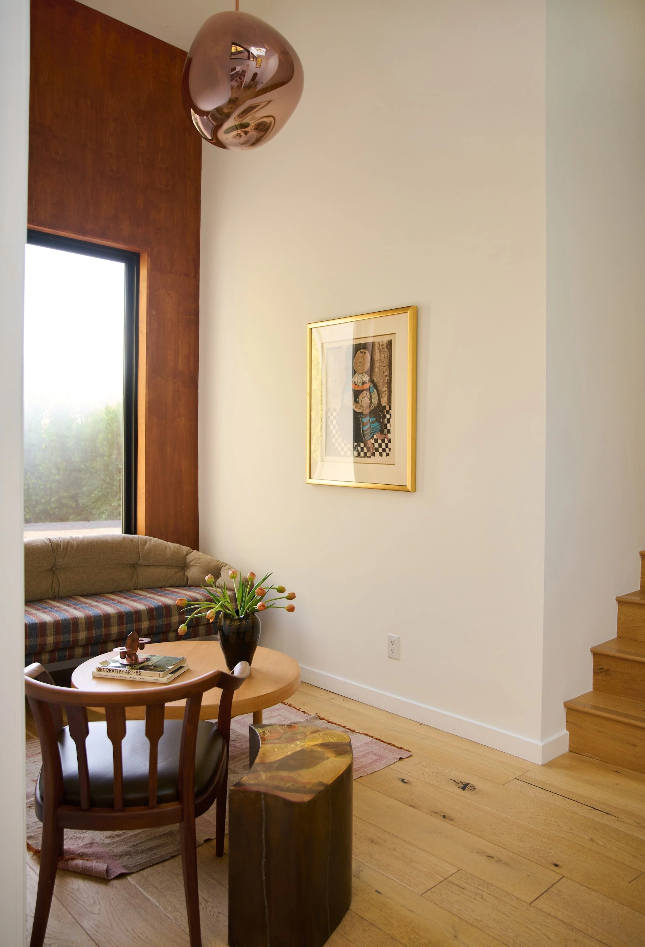 reading nook at base of stairs with terracotta colored wall, artwork, window seat, round coffee table, armchair, and side table