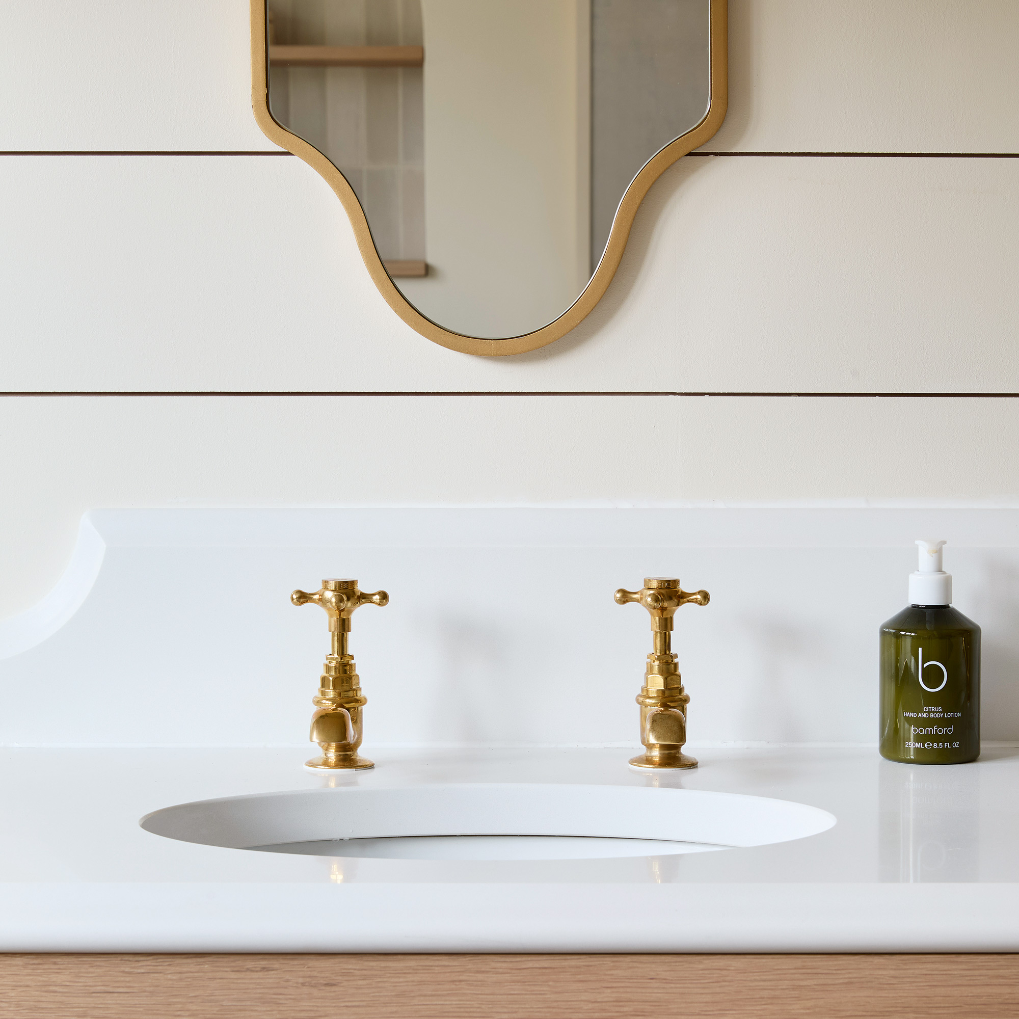 close up of a neutral bathroom with horizontal wall panelling, a white basin, brass taps and a matching mirror
