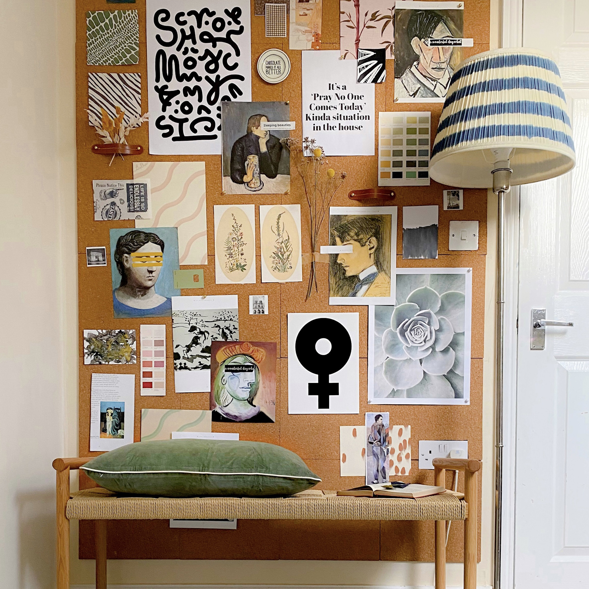 Cork surface on the wall behind a small woven bench, decorated with a mix of postcard, paint swatches and A4 prints