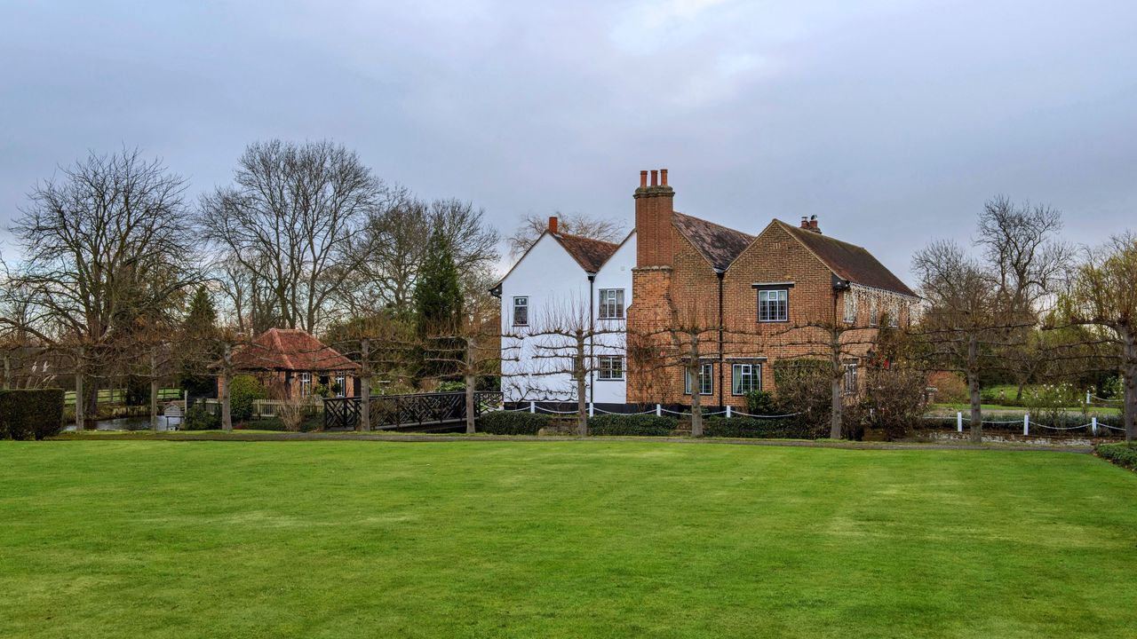 Large green grass lawn in front of row of espalier trees and house in winter garden