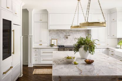 kitchen with white and neutral colors and large island with quartz countertop and white cabinets and two brass hoop pendant lights above island