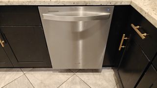 Stainless Steel Whirlpool dishwasher installed among black cabinets with a marble countertop and tile floor