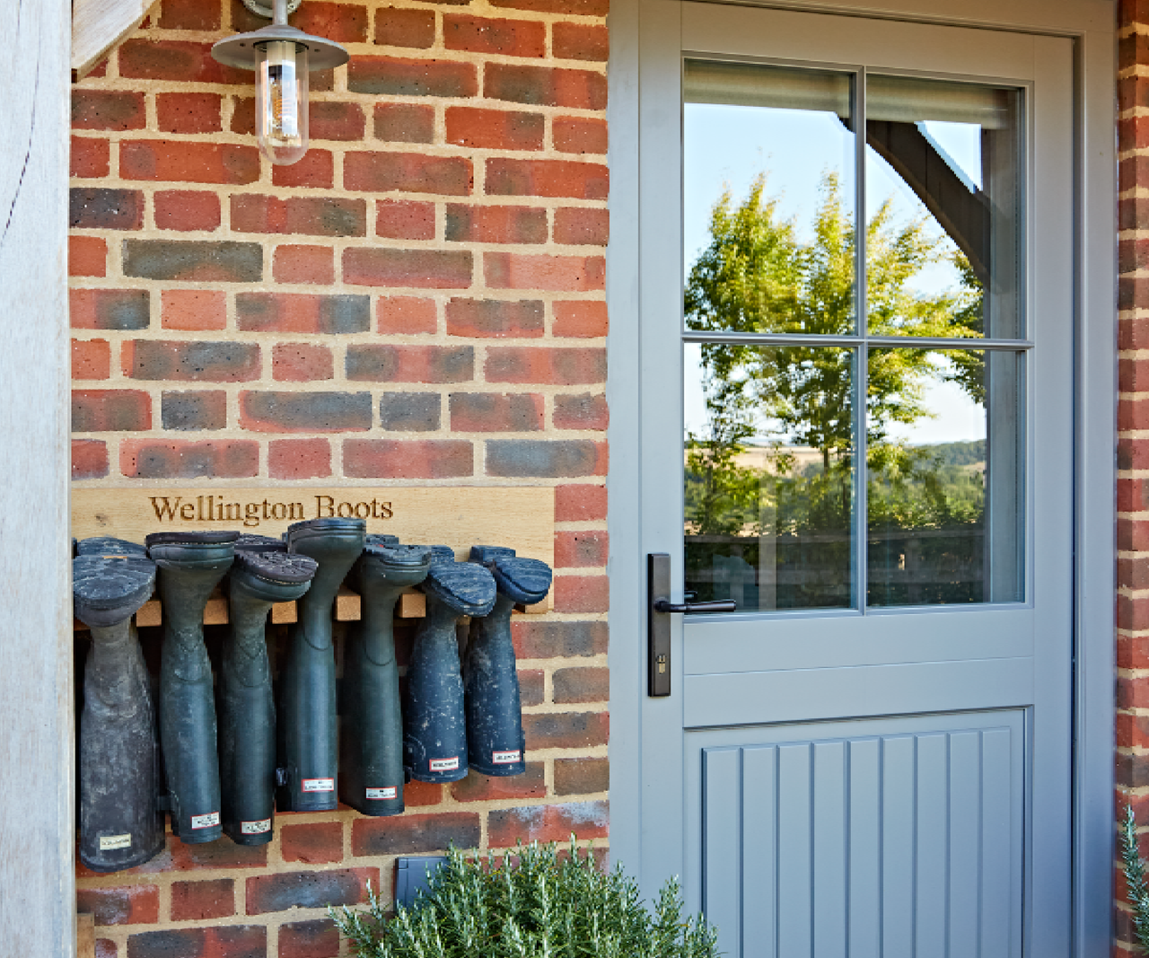 Front door with welly boots lined up on wooden plank on brick wall