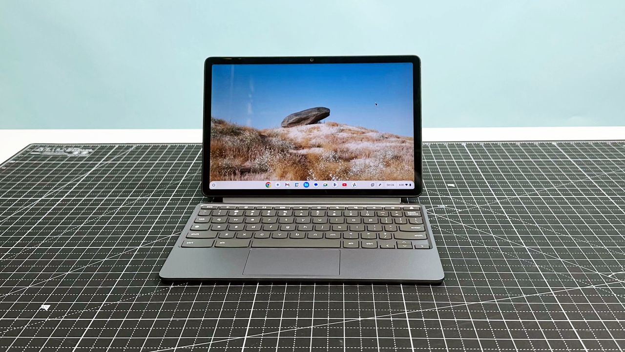 The Lenovo Chromebook Duet 11 Gen 9 facing forward on a white desk and black mat, with a blue backdrop.