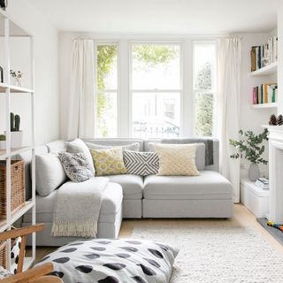 a living room with white wall ,grey sofa, white open shelf and grey carpet on floor