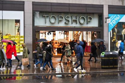 Pedestrians walking over wet pavement near Topshop store entrance