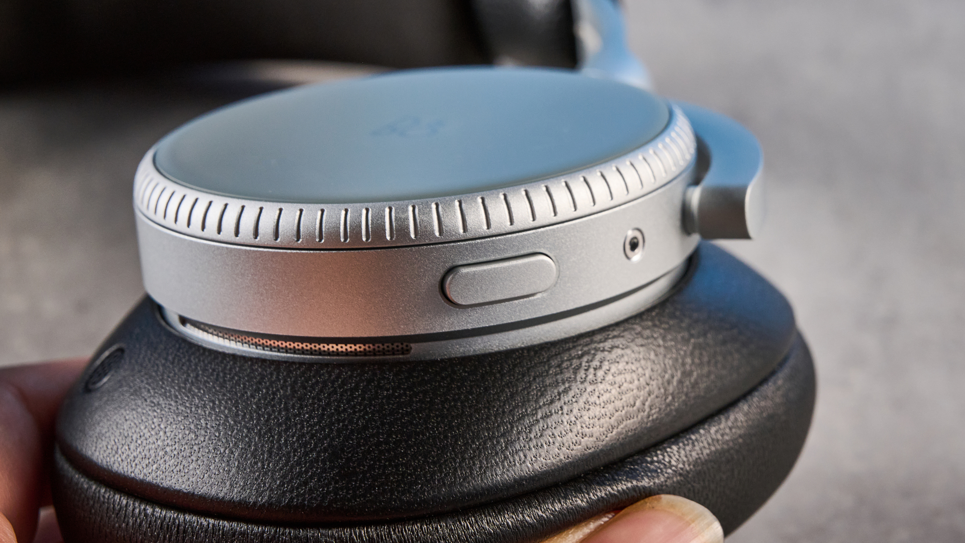 The Bang &amp;amp; Olufsen Beoplay H100 earcups in hand on a stone surface