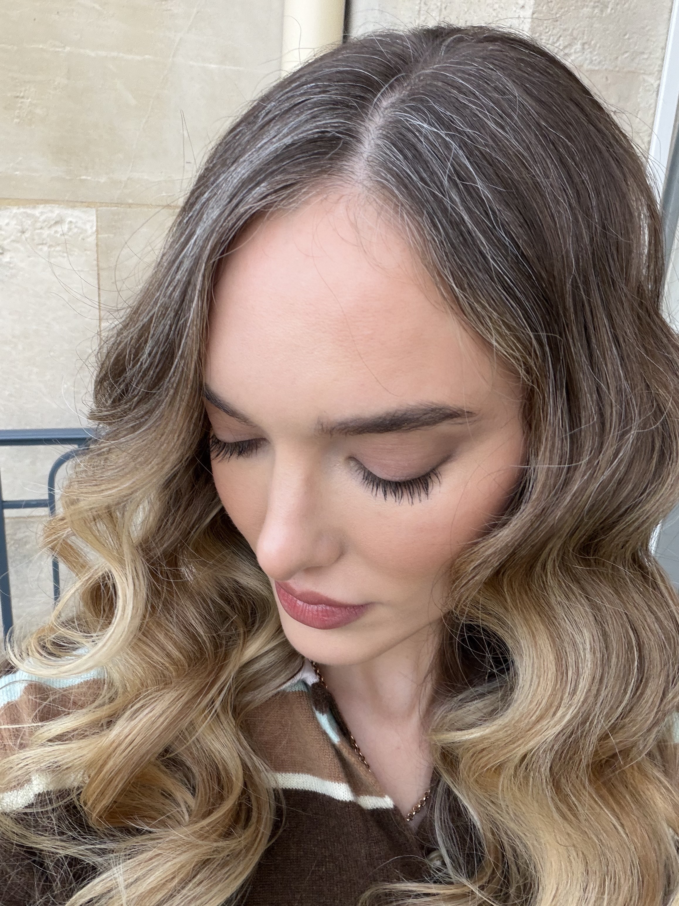 a woman with curly blonde hair with a gray streak with dark brows wearing a brown and white striped sweater