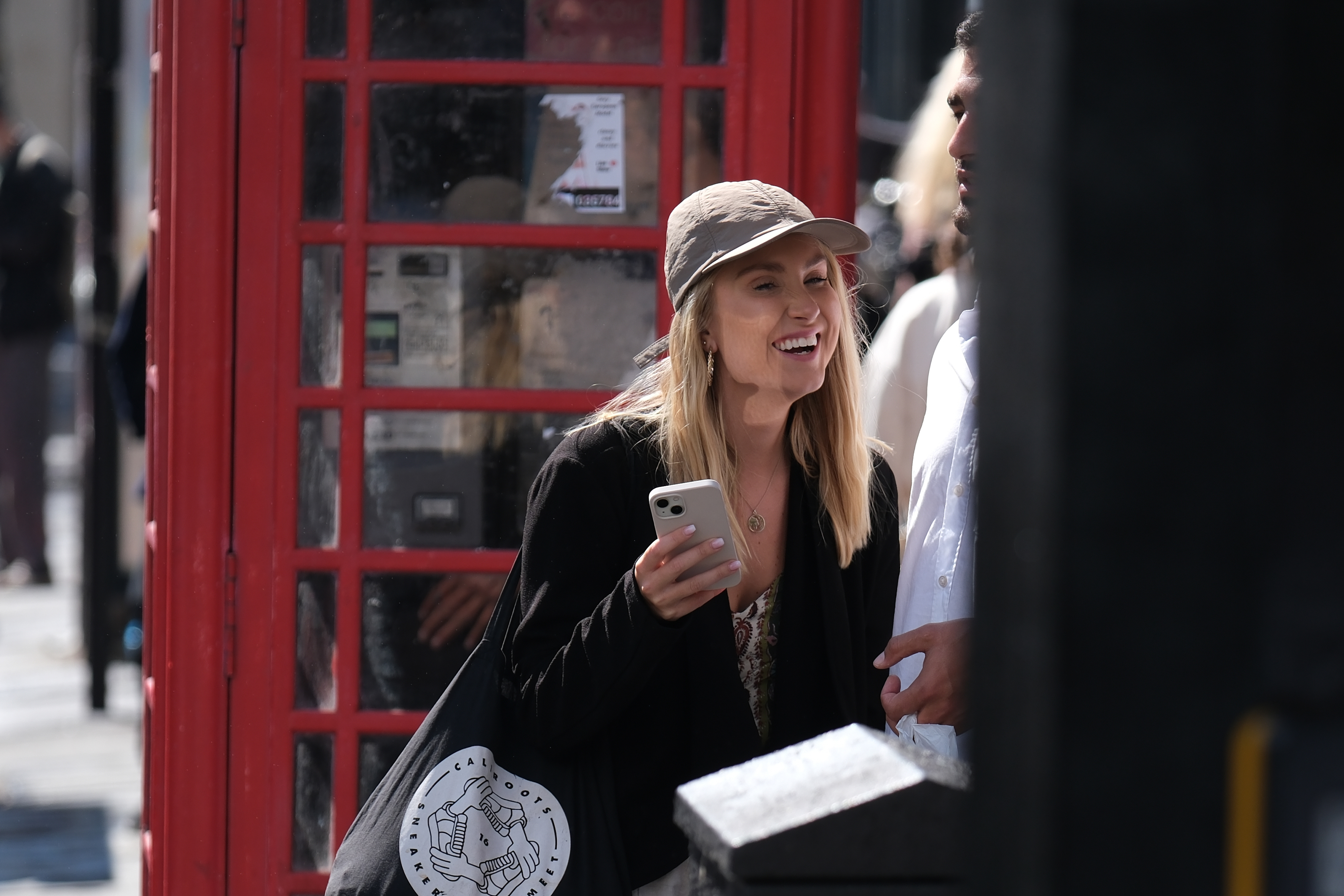 A woman holding a phone and laughing on a London street