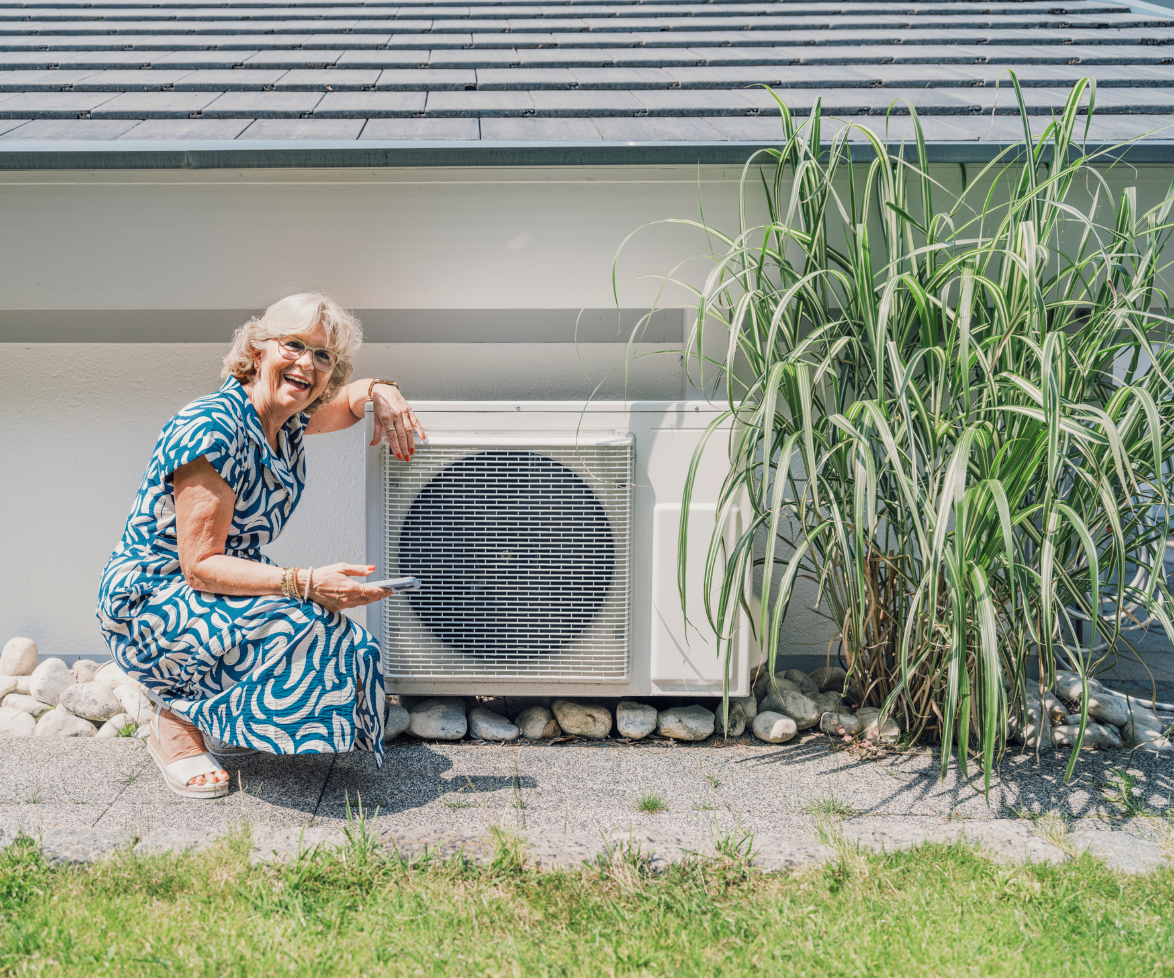 female crouched down smiling next to heat pump outside a home