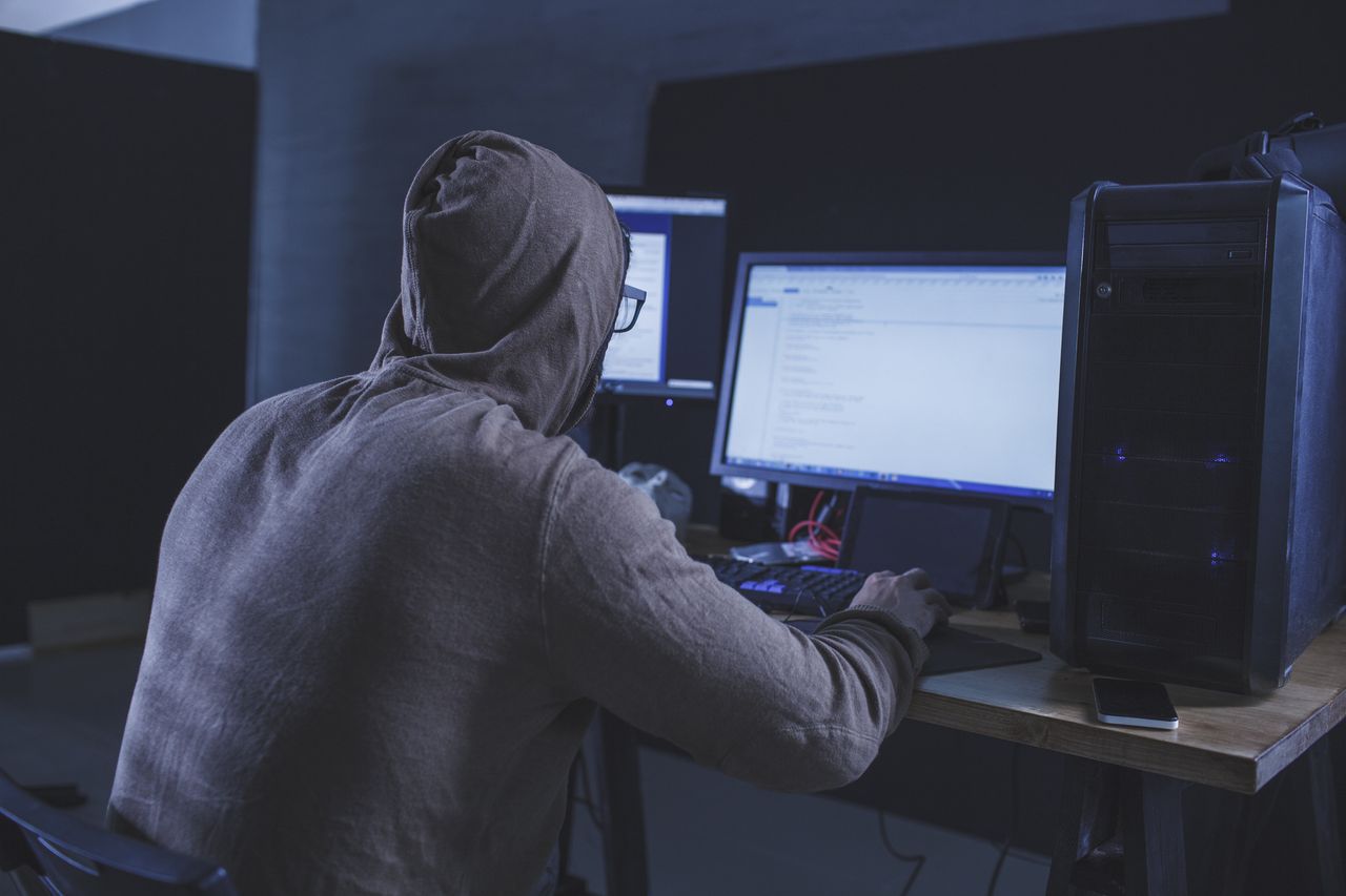 Computer hacker wearing hooded shirt using computer at table