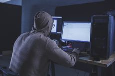 Computer hacker wearing hooded shirt using computer at table