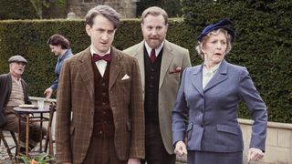 James Anthony-Rose in a tweed jacket as Carmody stands next to Samuel West in a tweed jacket as Siegfried and Patricia Hodge in a blue suit as Mrs Pumphrey all looking surprised in All Creatures Great and Small.