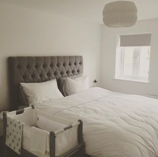 'Before' shot of bedroom with white walls, grey fabric headboard, white bedding and grey and white cot