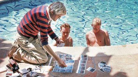 British painter, draughtsman, printmaker, stage designer and photographer David Hockney, poolside in Los Angeles, with polaroids of David Stoltz & Ian Falconer, circa 1978. (Photo by Michael Childers/Corbis via Getty Images)