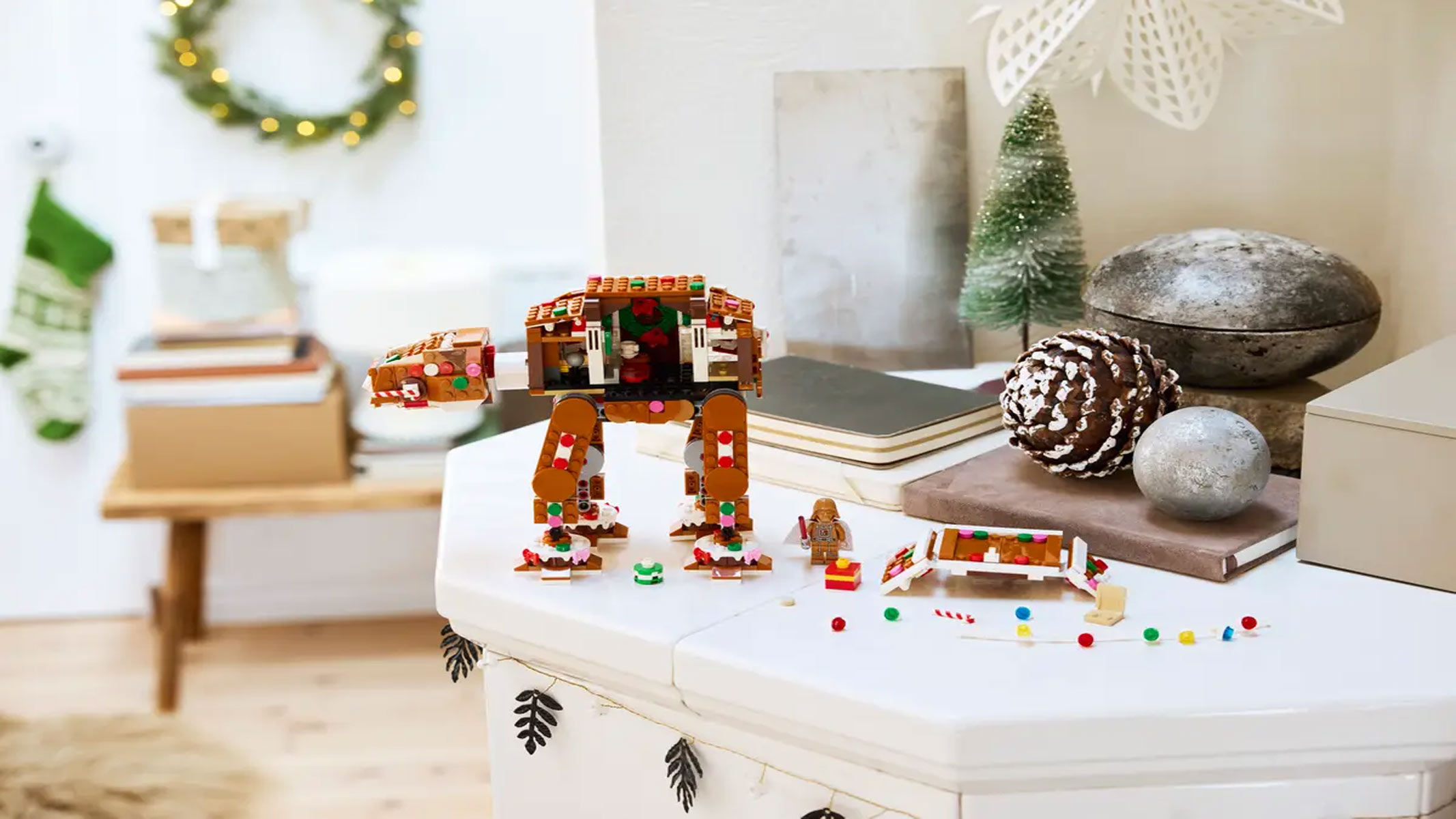 A Gingerbread-colored camel-like robot has a side panel opened up to expose a festive interior with several smaller parts displayed in front of the robot, all on a white surface.