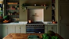 traditional green kitchen with marble counter, open shelving, aga stove, timber island bench with vegetables on it