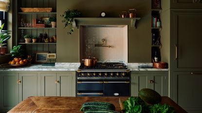 traditional green kitchen with marble counter, open shelving, aga stove, timber island bench with vegetables on it