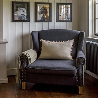grey armchair with light coloured cushion and throw on wooden flooring in front of a light grey wall with picture gallery