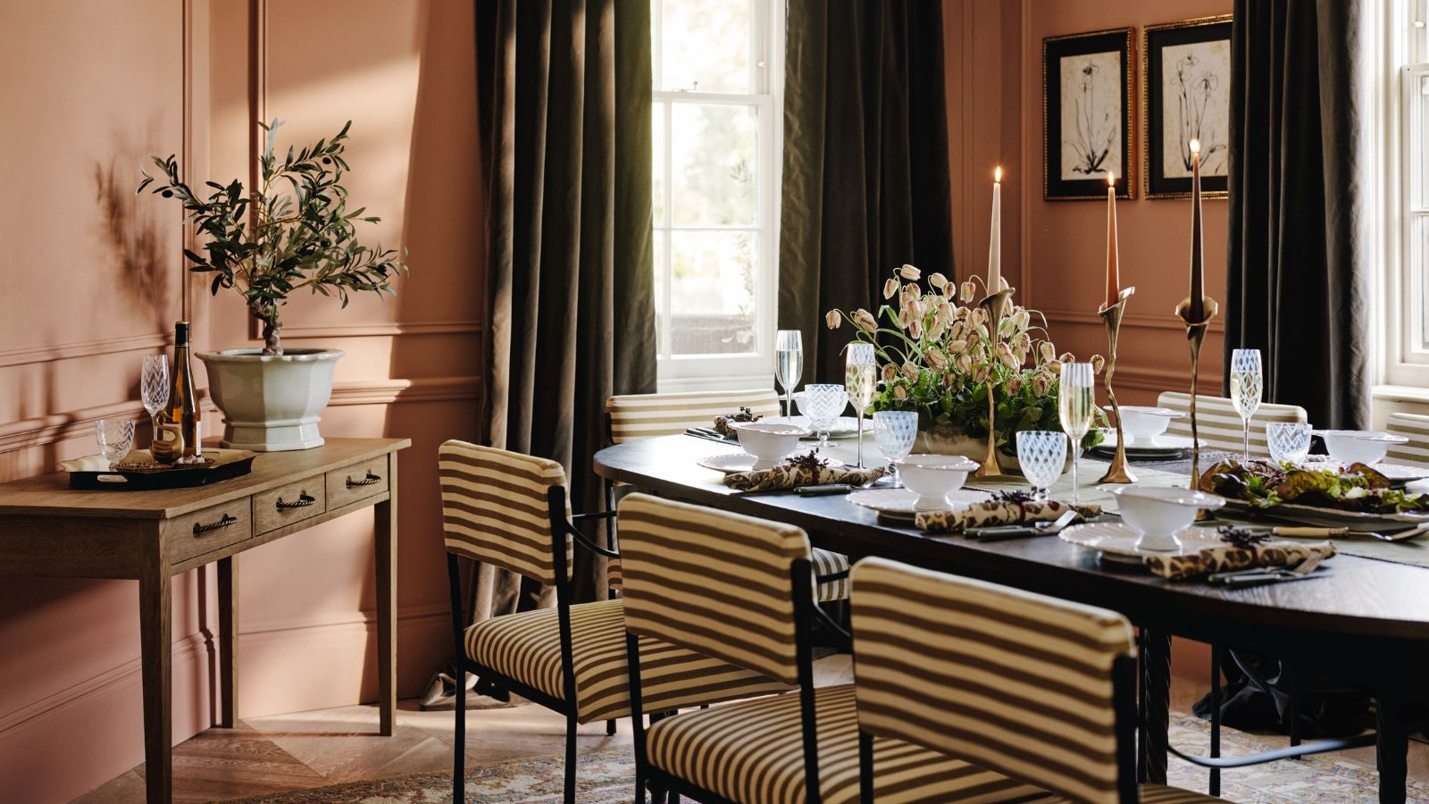 A pink dining room with a long black table surrounded by green and white striped chairs 