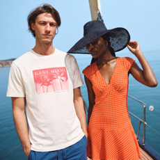 A male and female model stood on a boat overlooking the sea wearing a white GANT t-shirt and a polkadot dress sold at Secret Sales
