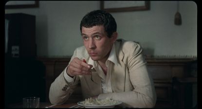Film still from La Chimera movie showing actor Josh O’Connor in a suit eating pasta