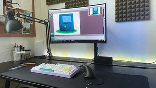 A black desk with a keyboard, lamp, HP 925 ergonomic vertical mouse, and a monitor showing the Asperite drawing app
