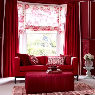 living room with red wall red sofa with designed cushion and window with red curtain