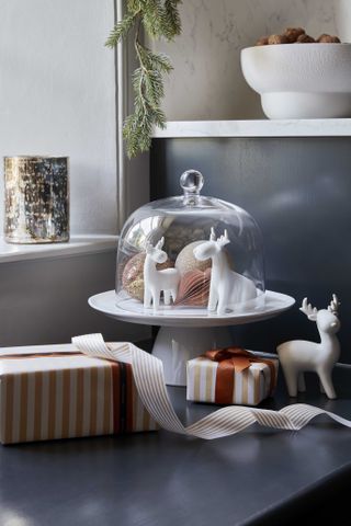 cake stand with reindeers and baubles, presents on the side, tealight holder, bowl with walnuts on a dark countertop