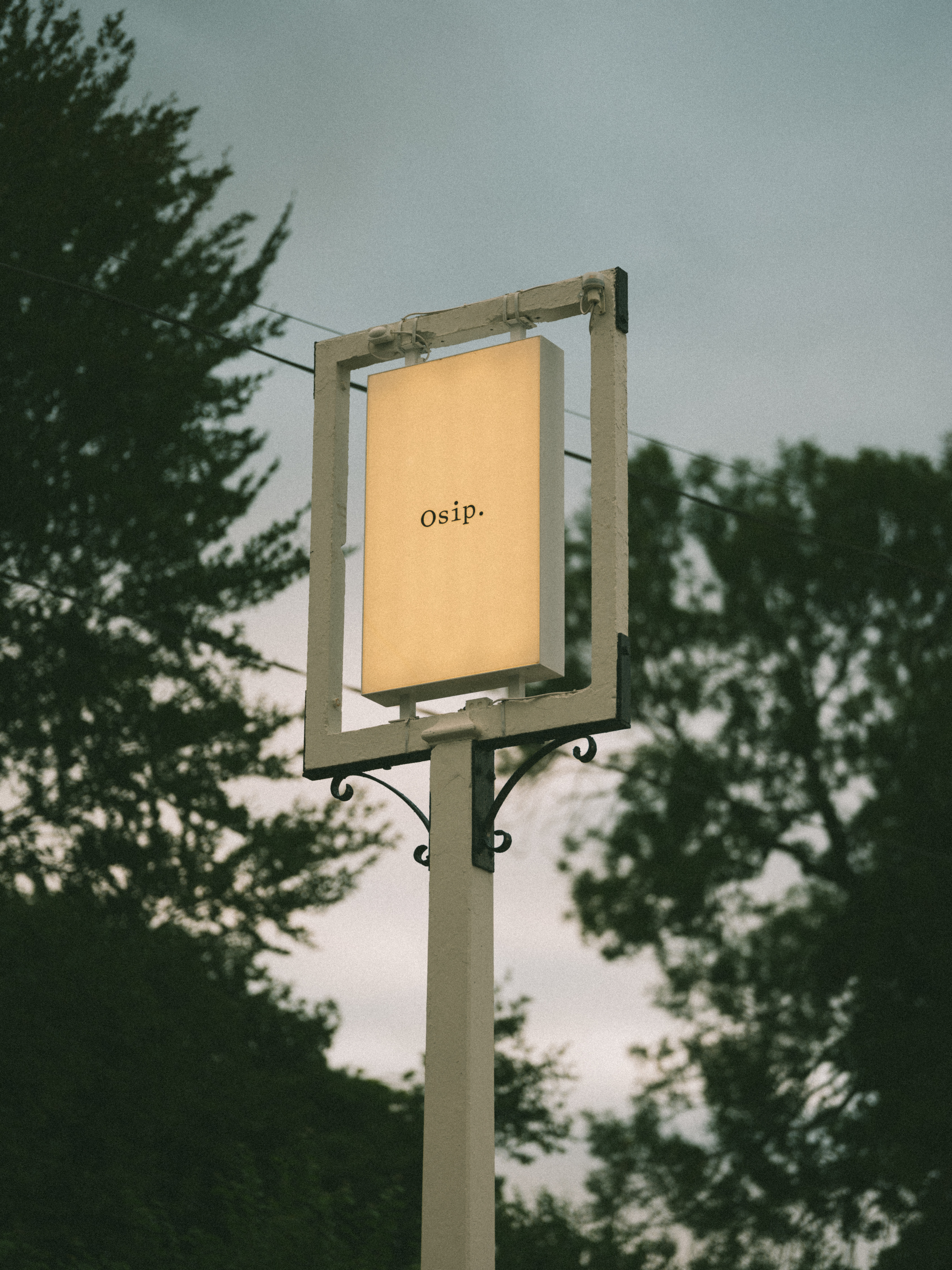 An old road sign to a pub now filled with a minimalist, back-lit sign that reads &quot;Osip.&quot; in black against a white background.