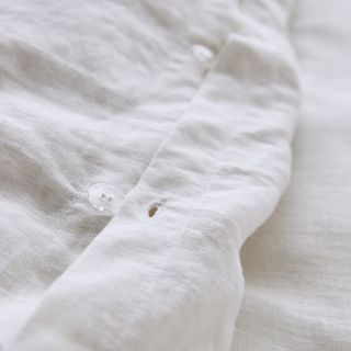 A close up of a white linen duvet cover showing a clear plastic button and button hole