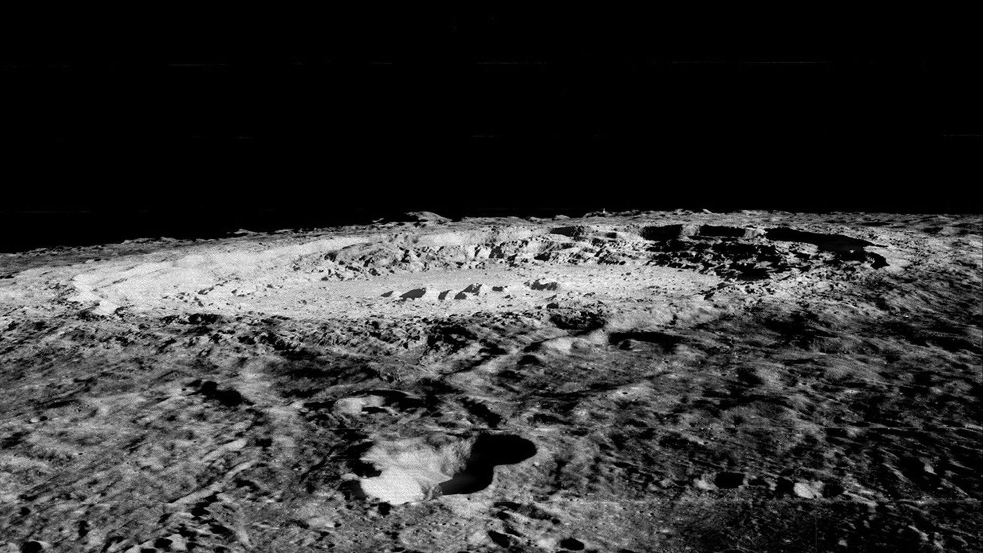 A black and white image of the moon&#039;s surface. There is a huge crater there.