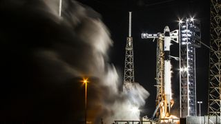 A black and white SpaceX Falcon 9 rocket fires its engines in a test on a launch pad for Crew-9