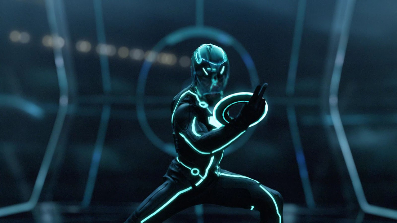 Screenshot from the movie Tron: Legacy. A person is wearing a black bodysuit and helmet, both with blue light trim. They are holding up a disc with a blue circle on it, preparing to throw it.