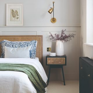 A bedroom with a rattan headboard on the bed and a rattan-insert bedside table with a vase of flowers