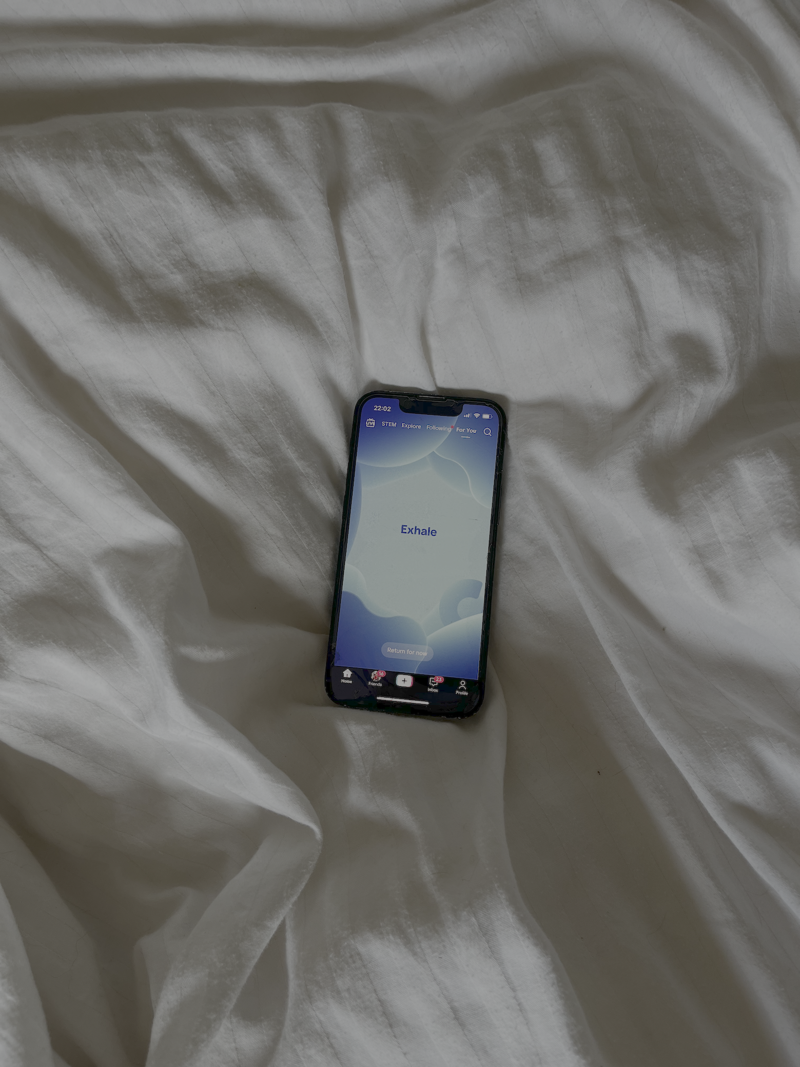 An iPhone lying on a bed with a lit up display showing a guided breathwork exercise