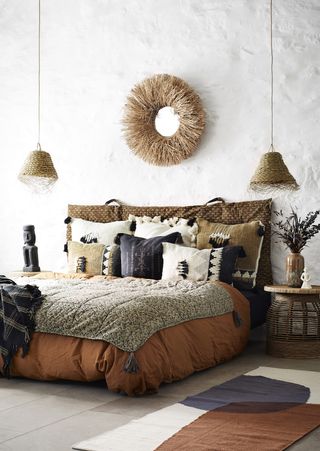 boho style bedroom with rattan hanging pendants, mirror, side tables, rug, tasselled throw, tasseled boho style cushions, vases