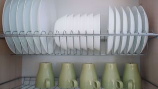 Plates and mugs stored on wires shelfs in kitchen cupboard