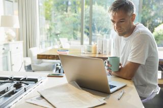 A man sitting at his kitchen counter with a mug of coffee and his laptop