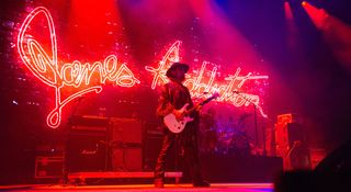 Dave Navarro stands onstage with the Jane's Addiction lighting up in red/punk neon behind him