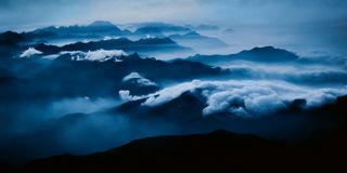 a landscape scene depicting mountains and clouds in a blue hue