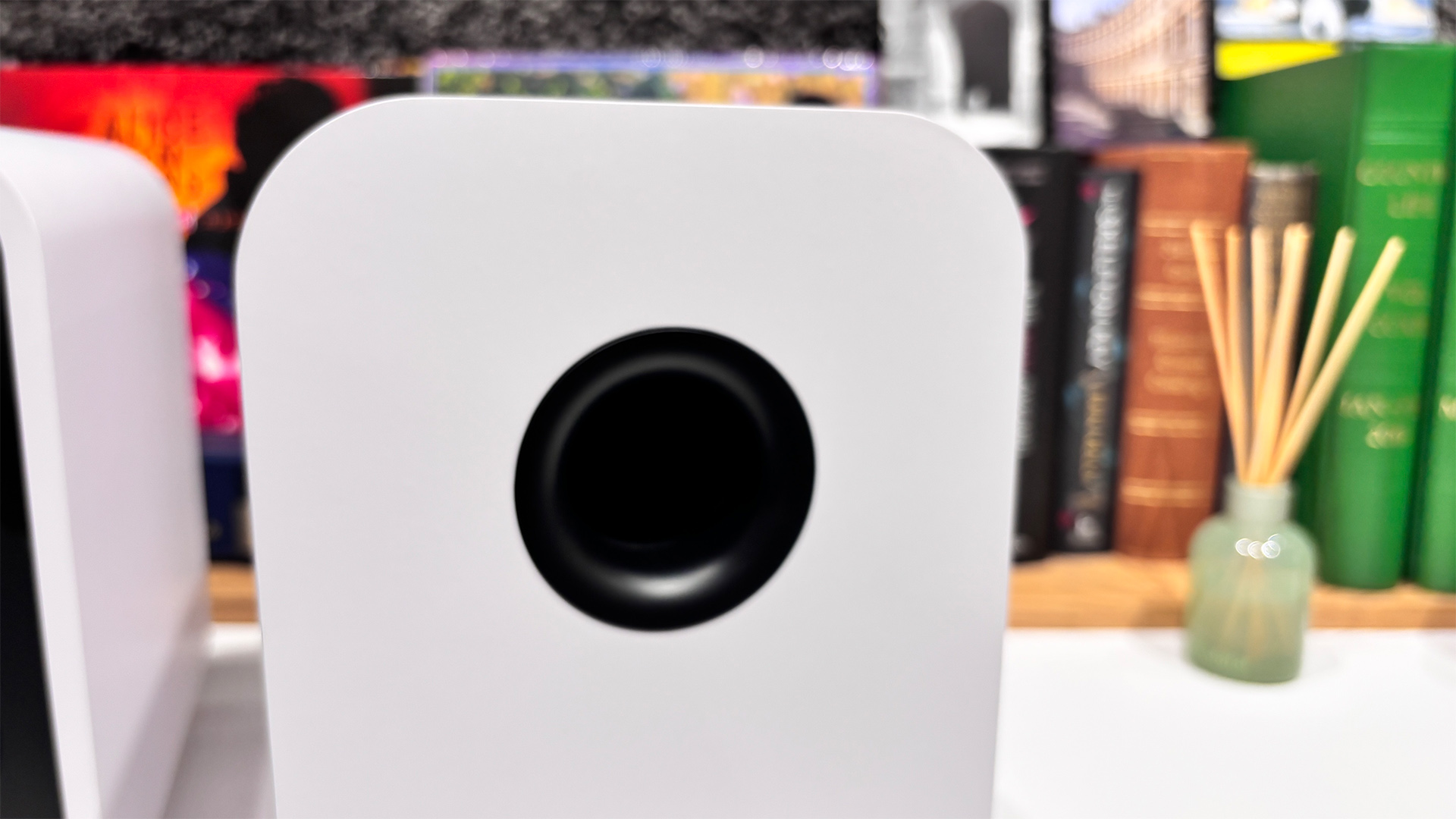 Q Acoustics 5010 standmount speakers on white surface in front of busy bookshelf, close up on rear port
