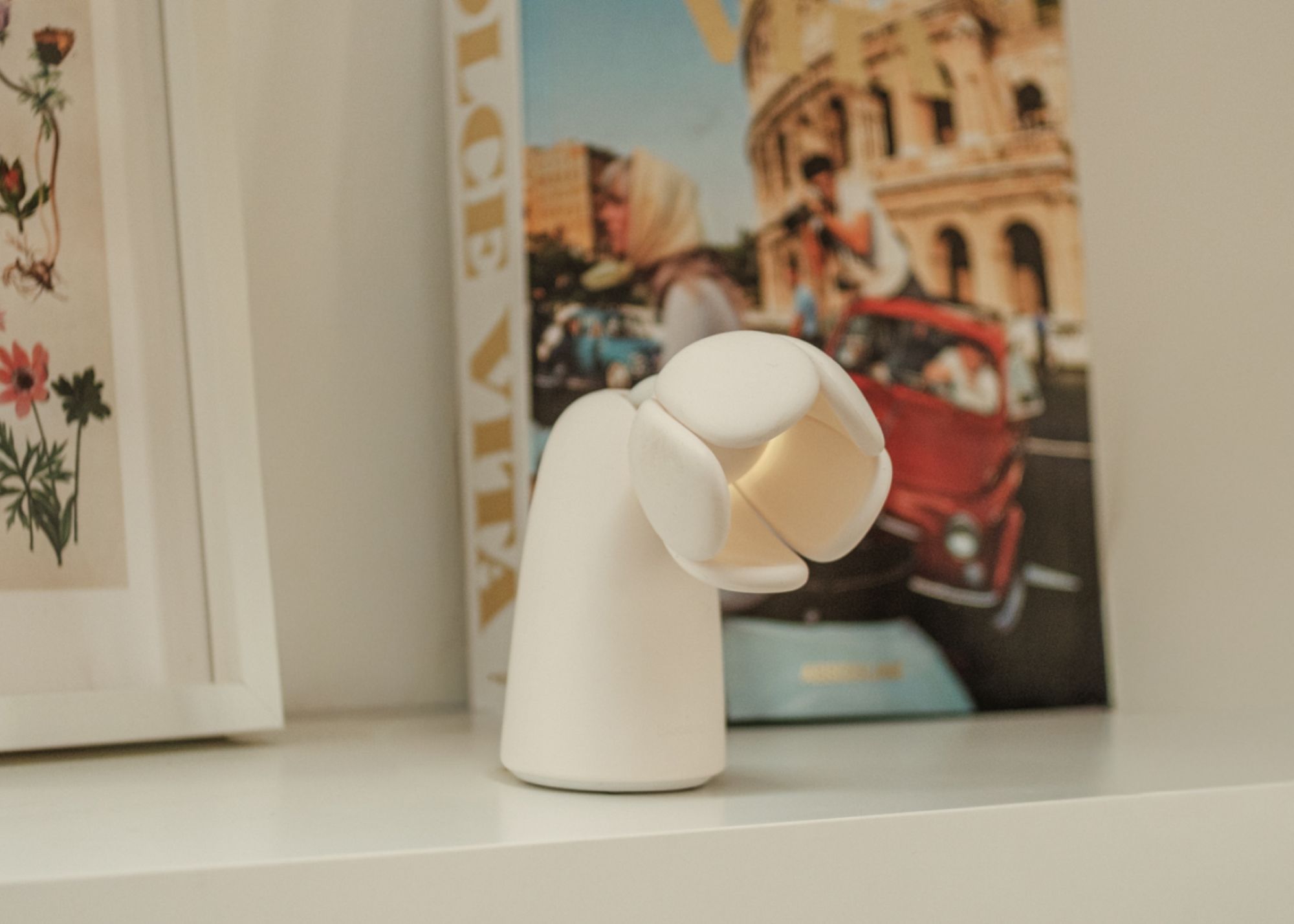 An off-white flower-shaped air quality checker from Bloomie on a shelf with colorful coffee table books