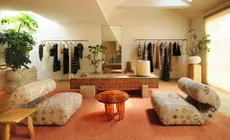 A desert-inspired luxury boutique features 70s plush furniture such as upholstered armchairs, futuristic wooden and resin tables, rock-made coffee tables, and thriving plants in an argilla-hued, sumptuous environment.