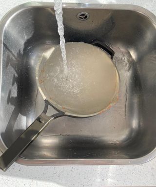 Rinsing an Our Place Always pan with running water from kitchen faucet